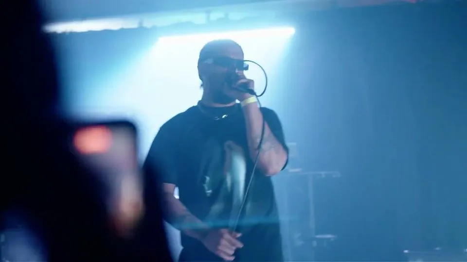 Al Bear on stage with a mic under blue light, from the Prayers on me video