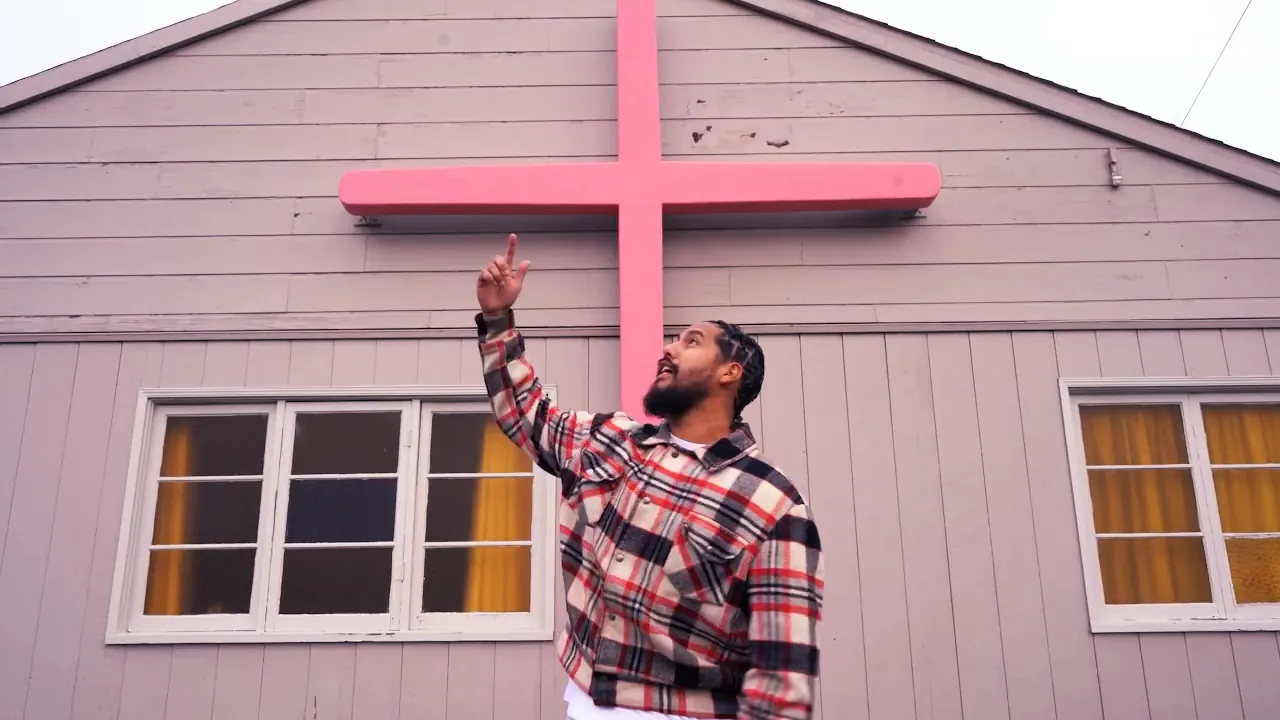 Al Bear pointing up at a pink cross on a wood house