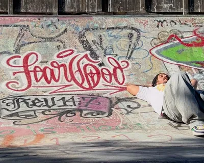 Al Bear lying on a skatepark bank beside Fear God graffiti